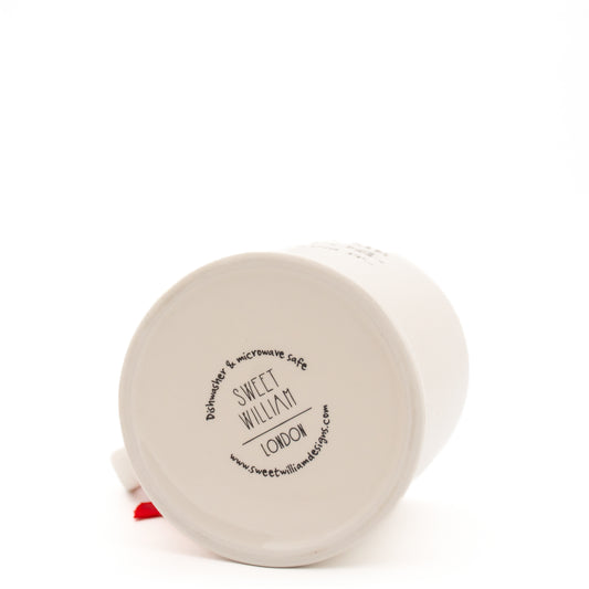 A white Sweet William mug, lying on its side with the base facing the camera. The base shows Sweet William London in black, with the website address and information about the mug being microwave and dishwasher safe in a circle around the brand name. The mug is shown on a white background.