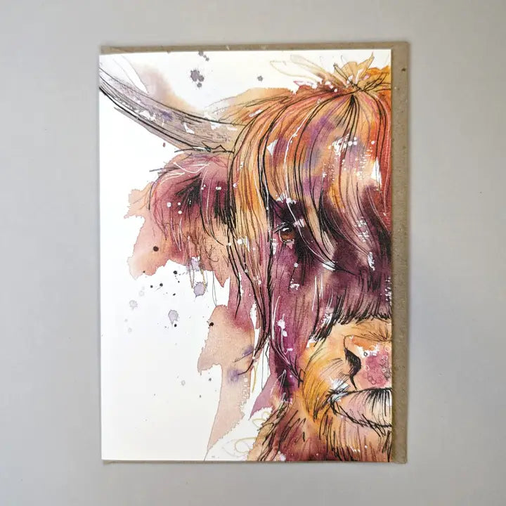Tori Ratcliffe Art Highland Cow card, showing half of the head of a light brown shaggy highland cow. The watercolours used as pinks, oranges, browns, greys and purples, with the significant features highlight with black fine pen. The highland cow sits on a white background. The card is also on a white background with a brown envelope protruding out the right hand side of the card.
