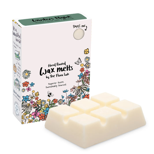 The Flora Lab Winter’s Night scented wax melt box with a dark green top and floral decorations on the bottom front edge stood in front of a white slab of wax melts. They are placed on a white background