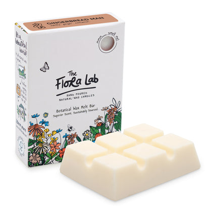 The Flora Lab Gingerbread Man Scented Wax Melts. A slab of white wax melts, unboxed in the foreground, with the white box (with floral decoration around the bottom) stood on end slightly behind and to the left.