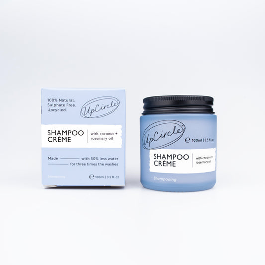 Upcircle Shampoo Crème in a blue jar with a black metal lid on the right. On the left a light blue box with details about the shampoo Crème. Both sat on a white background.